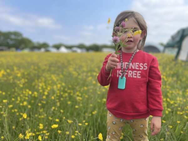 Child model in a field of buttercups wearing turquoise taggle chew necklace with infinity lanyard
