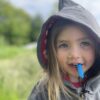 Child model wearing grey hoodie with blue zip chew in field