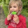 Child model in a field with green dinosaur chew necklace in her mouth
