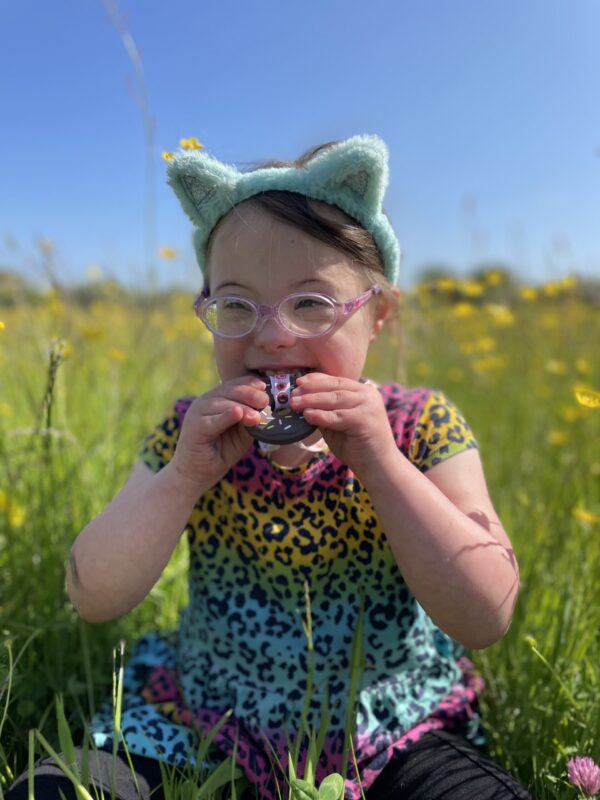 Child with Downs Syndrome in a field wearing a brown doughnut Chew Necklace with doughnuts lanyard