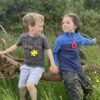 Two child models wearing a puzzle chew necklace and square chew necklace on lanyards sitting on farm equipment