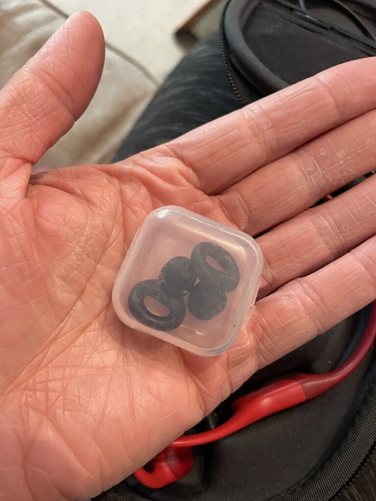 Hand holding a small plastic box containing black ear plugs