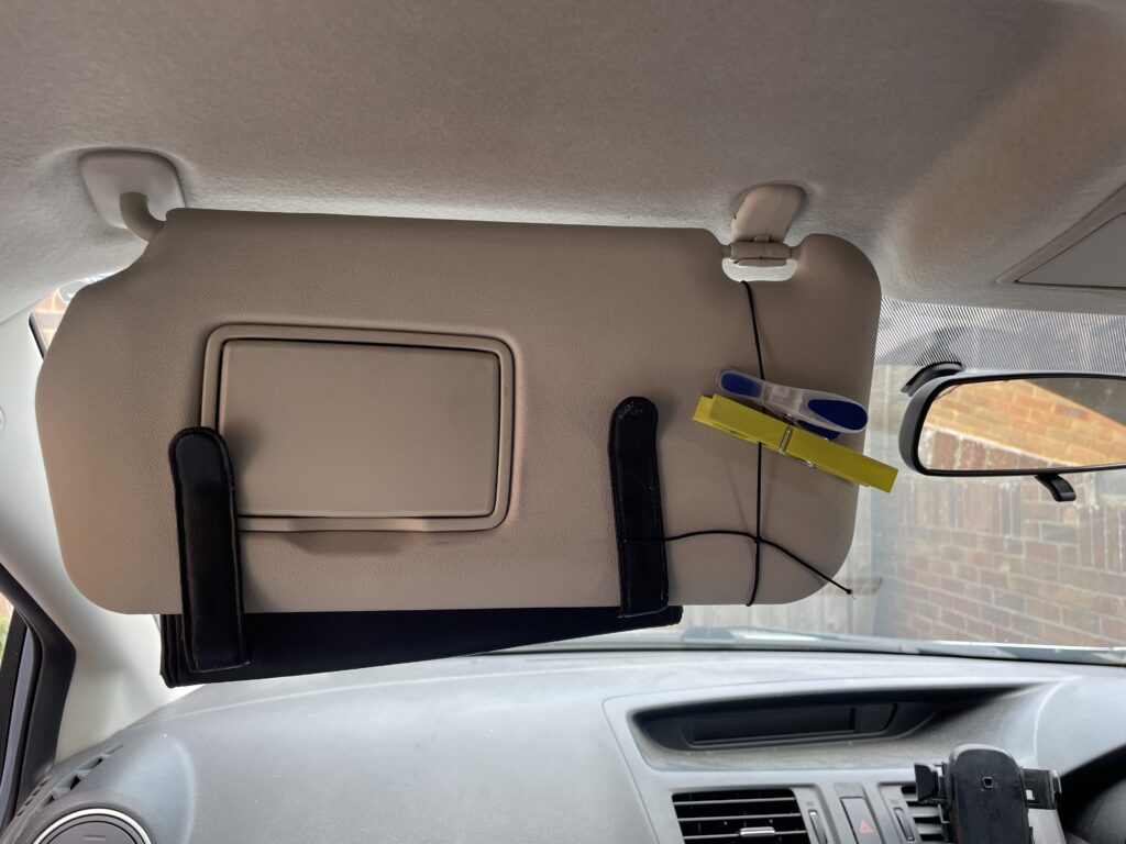 DIY sun visor setup in a car using a yellow and blue clip and black string