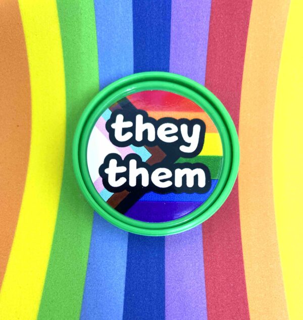 Pronoun pop badge with Pride flag backgrounds – they/them – from Sensory Oojamabobs on a rainbow striped background.